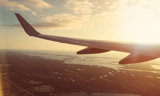 Blick aus einem Flugzeugfenster bei Sonnenuntergang, die Flügelspitze schwebt über einer weiten Landschaft. Perfekt als Leinwandbild oder Poster, um das Gefühl von Freiheit und Reisen in Ihr Zuhause zu bringen.