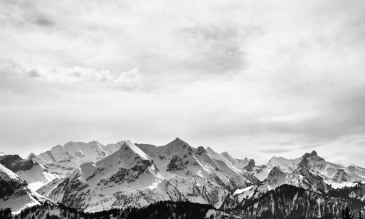 Schwarz-Weiß-Aufnahme von verschneiten Berggipfeln, die sich majestätisch in die Ferne erstrecken. Perfekt als Leinwandbild oder Poster, um die zeitlose Schönheit der Natur einzufangen.