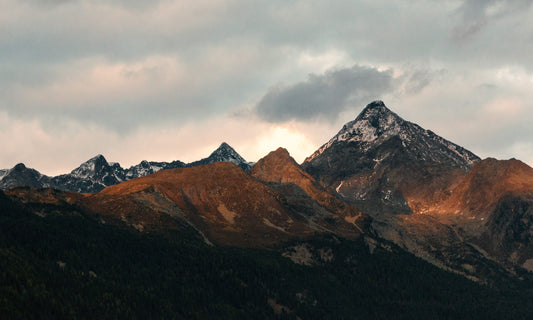 Ein beeindruckender Sonnenaufgang in den Bergen mit schneebedeckten Gipfeln, die in warmes Licht getaucht sind. Perfekt als Leinwandbild oder Poster, um die Magie der Natur in Ihr Zuhause zu bringen.